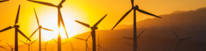 Wind turbines are silhouetted against a yellow sunset.